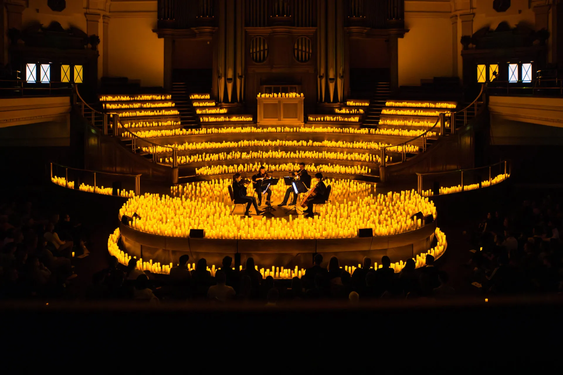 Central Hall WestminsterのGreat Hallで、キャンドルに囲まれた円形のステージで演奏する弦楽四重奏団。バルコニーからの眺めで、背後のオルガンへ向かってキャンドルが段々に並び、下の暗がりに観客がいる