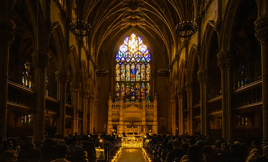 Candlelightコンサート中のブルックリン・ハイツのSt. Ann & the Holy Trinity Churchの身廊。信者席の観客、キャンドルが灯る通路、祭壇上のステンドグラスが見える