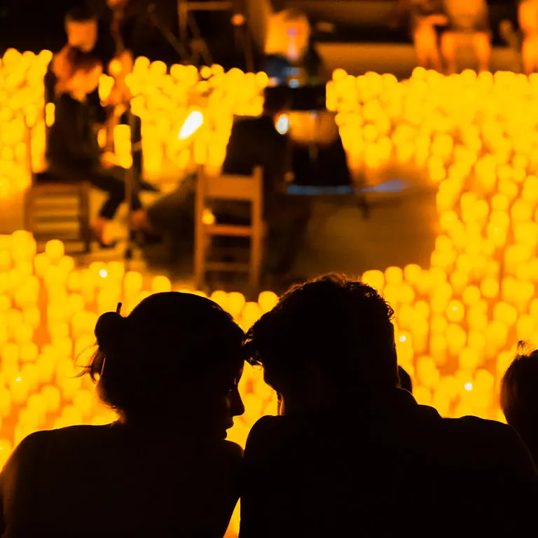 Two audience members watching a string quartet play inside a field of candles, from Fever's listing for the Candlelight concerts at Mead Garden