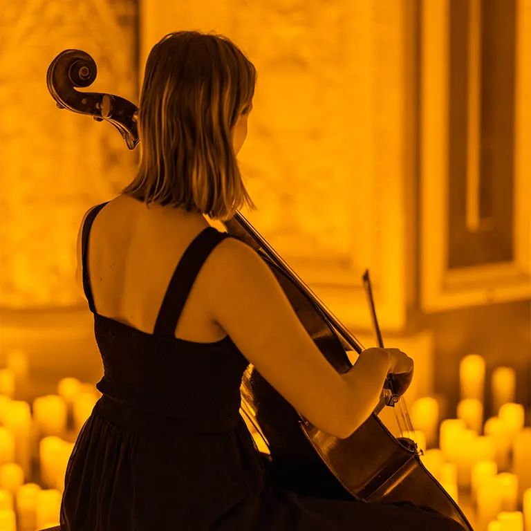 A cellist seen from behind, playing among flameless candles at a Candlelight concert