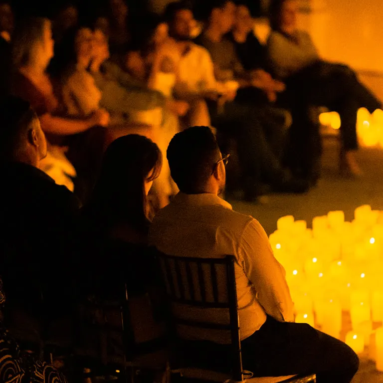 The audience seated in rows in candlelight, watching a concert