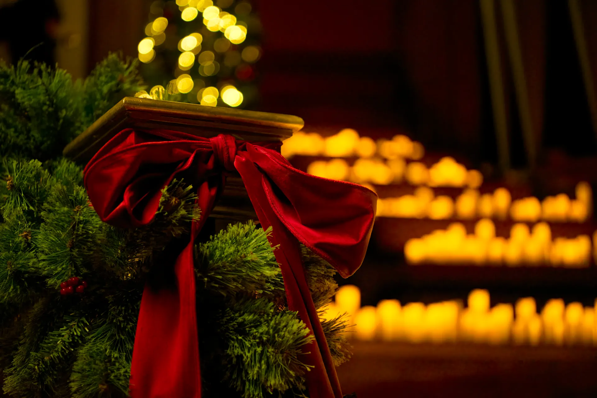 Central Hall WestminsterのクリスマスのCandlelightコンサートで、松と赤いベルベットのリボンを巻いた手すり。背後にはぼやけたキャンドルの灯りが並ぶ