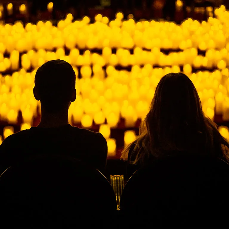 Two guests in silhouette seated before tiers of glowing candles at a Candlelight concert