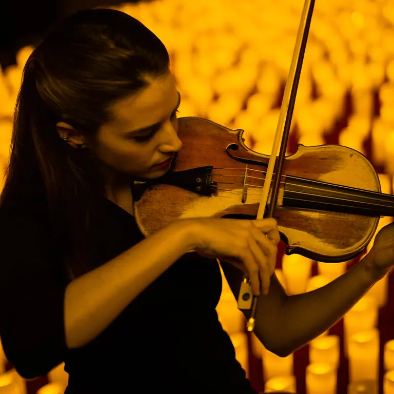 A violinist playing in front of a bank of flameless candles
