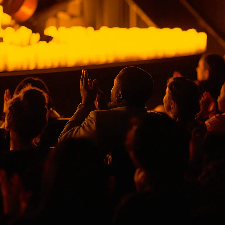 Audience members applauding below a gallery lined with candles at the end of a Candlelight concert