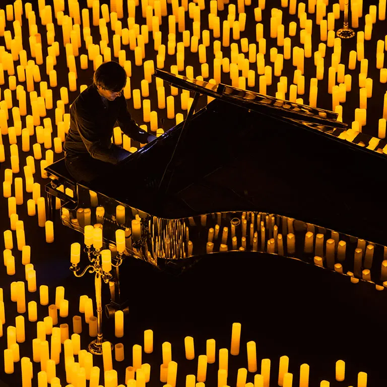 A pianist plays a grand piano surrounded on every side by hundreds of lit candles, seen from above
