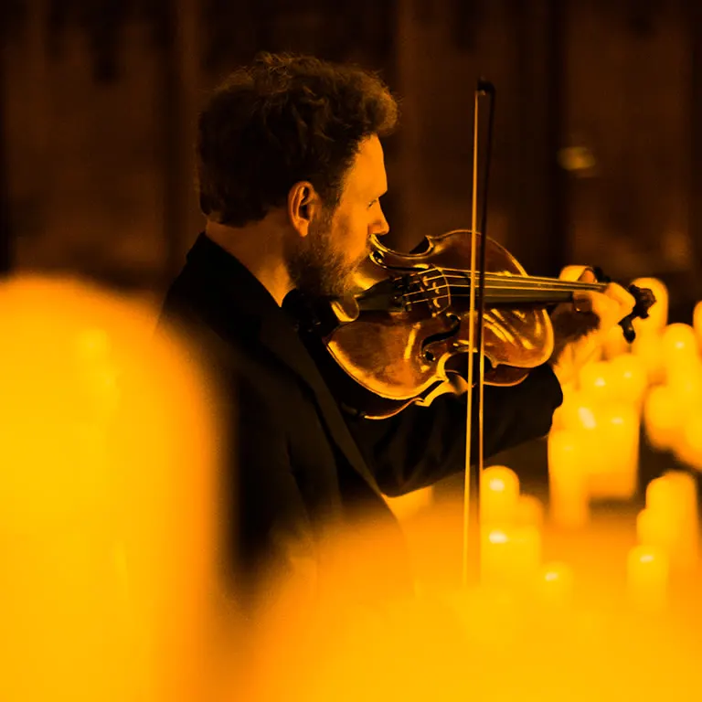 A violinist playing behind a row of flameless candles at a Candlelight concert