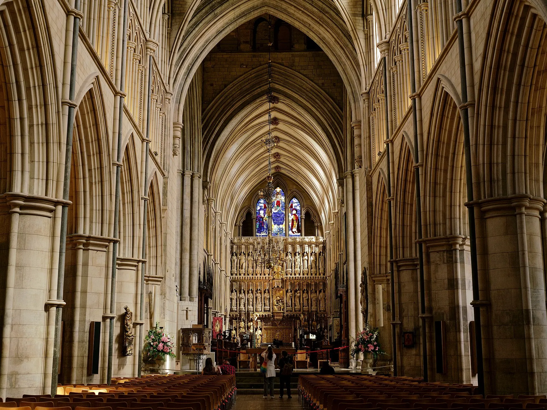 昼のSouthwark Cathedralのゴシック様式の身廊。淡い色の石のアーチの間に椅子の列が並び、奥に彫刻のある祭壇衝立と東側の窓が見える
