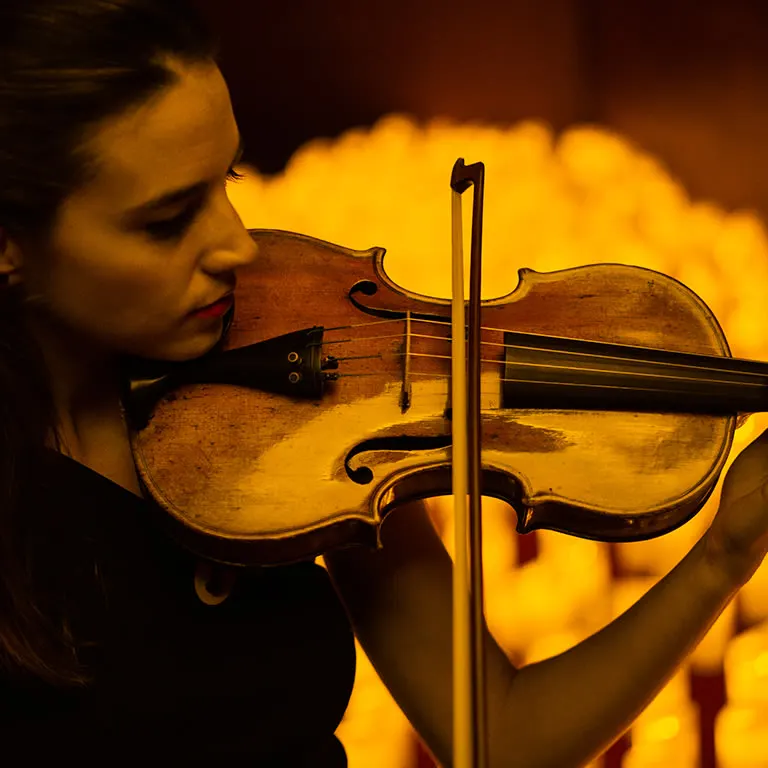 A violinist playing in front of a bank of glowing candles at a Candlelight concert