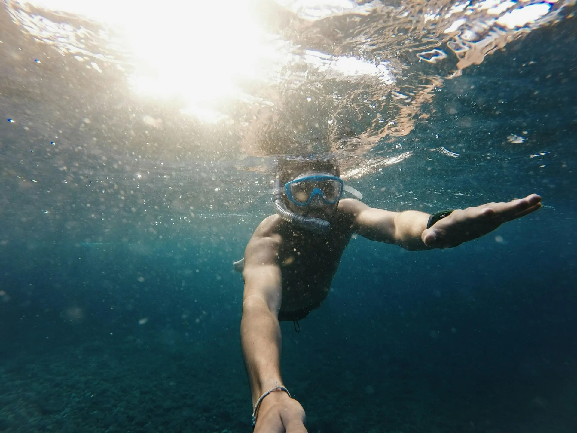 A snorkeller in a mask swimming underwater, with sunlight breaking through the surface above