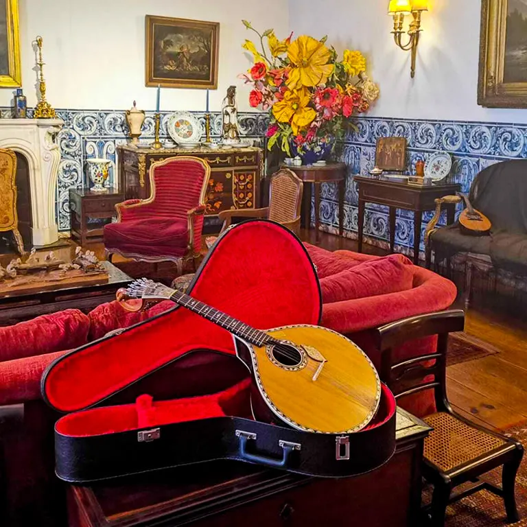 The salon of the Casa-Museu Amália Rodrigues, with blue and white azulejo panels, red armchairs, a vase of flowers and a Portuguese guitar in an open red case