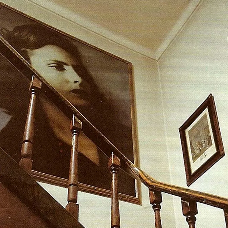 A large black and white portrait of Amália Rodrigues on the wall above the house's wooden staircase
