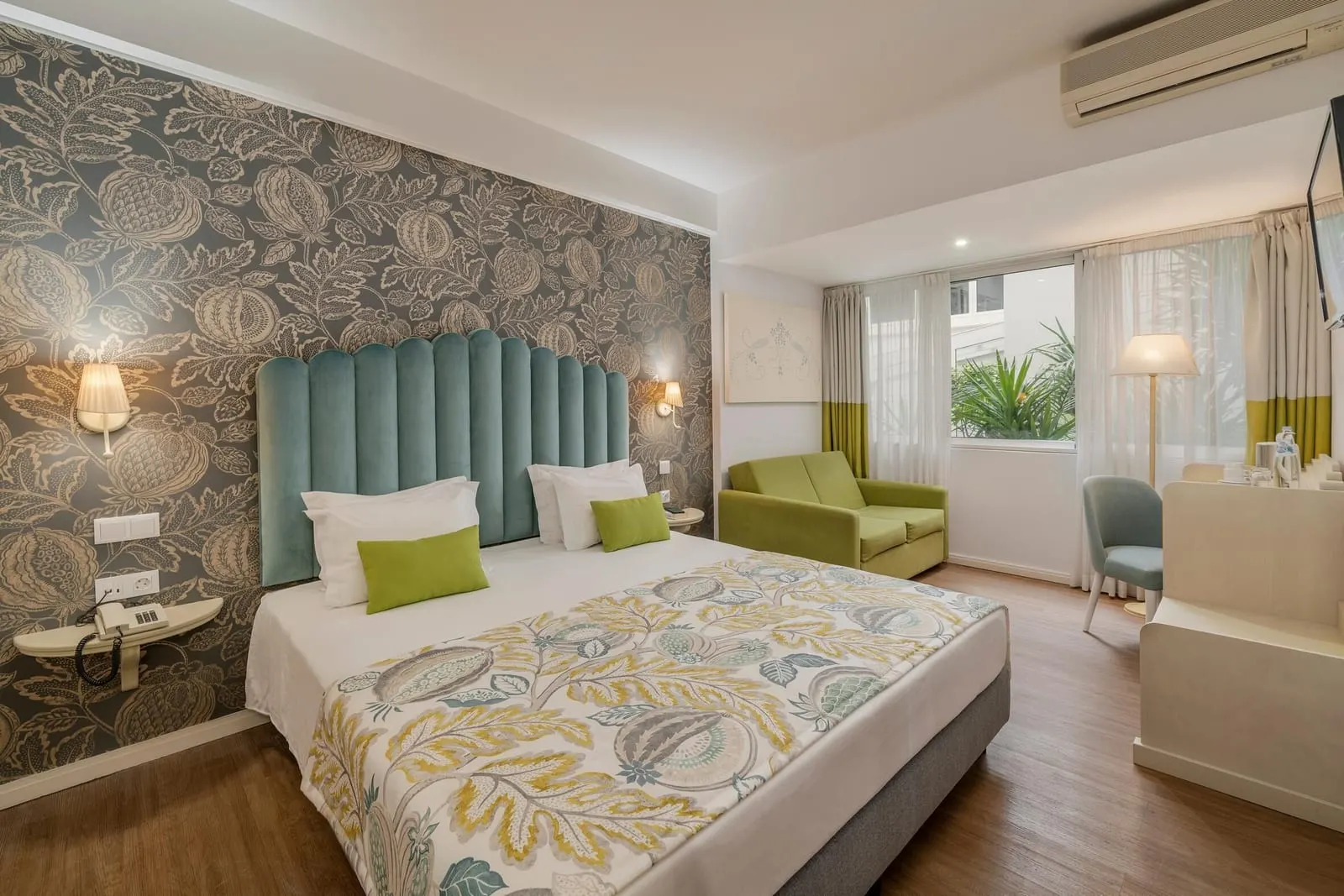 Standard Connecting Room im Hotel Madeira: ein Doppelbett mit geblümtem Überwurf vor einer Tapete mit Pflanzenmotiven und ein grünes Sofa an den Fenstern