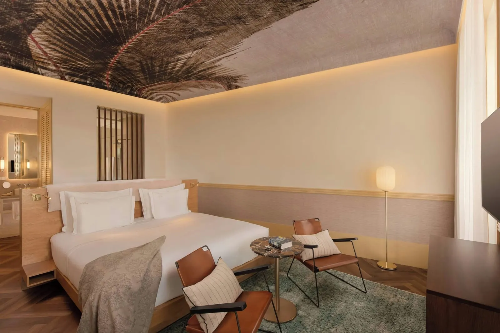 Premium room at The Ivens: the bed, two leather lounge chairs and a side table under a palm-leaf ceiling