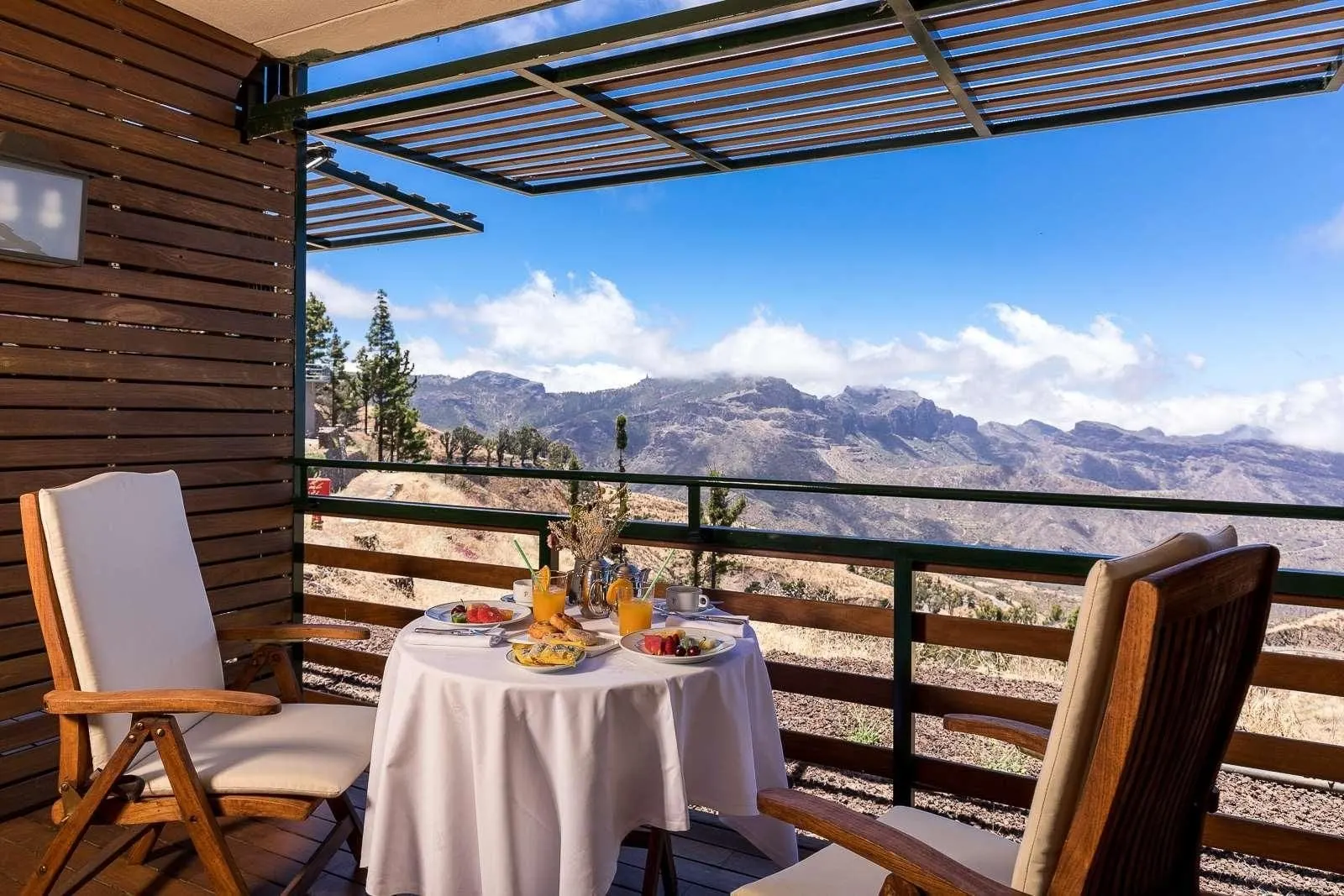 Standard Double at Parador de Cruz de Tejeda: a terrace under a slatted wooden pergola, with a round table set with fruit, pastries and juice between two cushioned wooden chairs