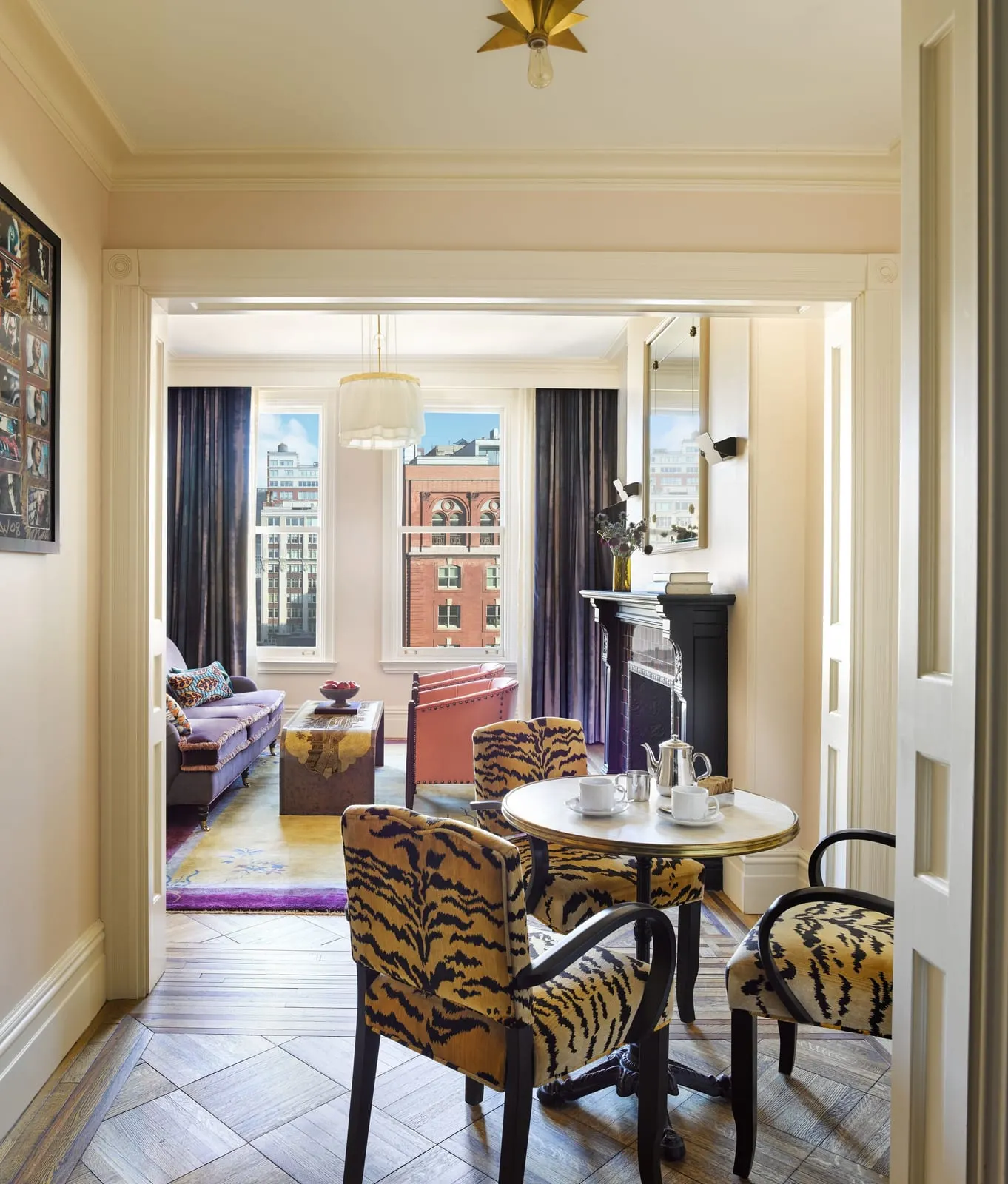 Chelsea Suite at Hotel Chelsea: a round table with tiger-print chairs and a tea set, opening onto a living room with a purple sofa and two pink armchairs