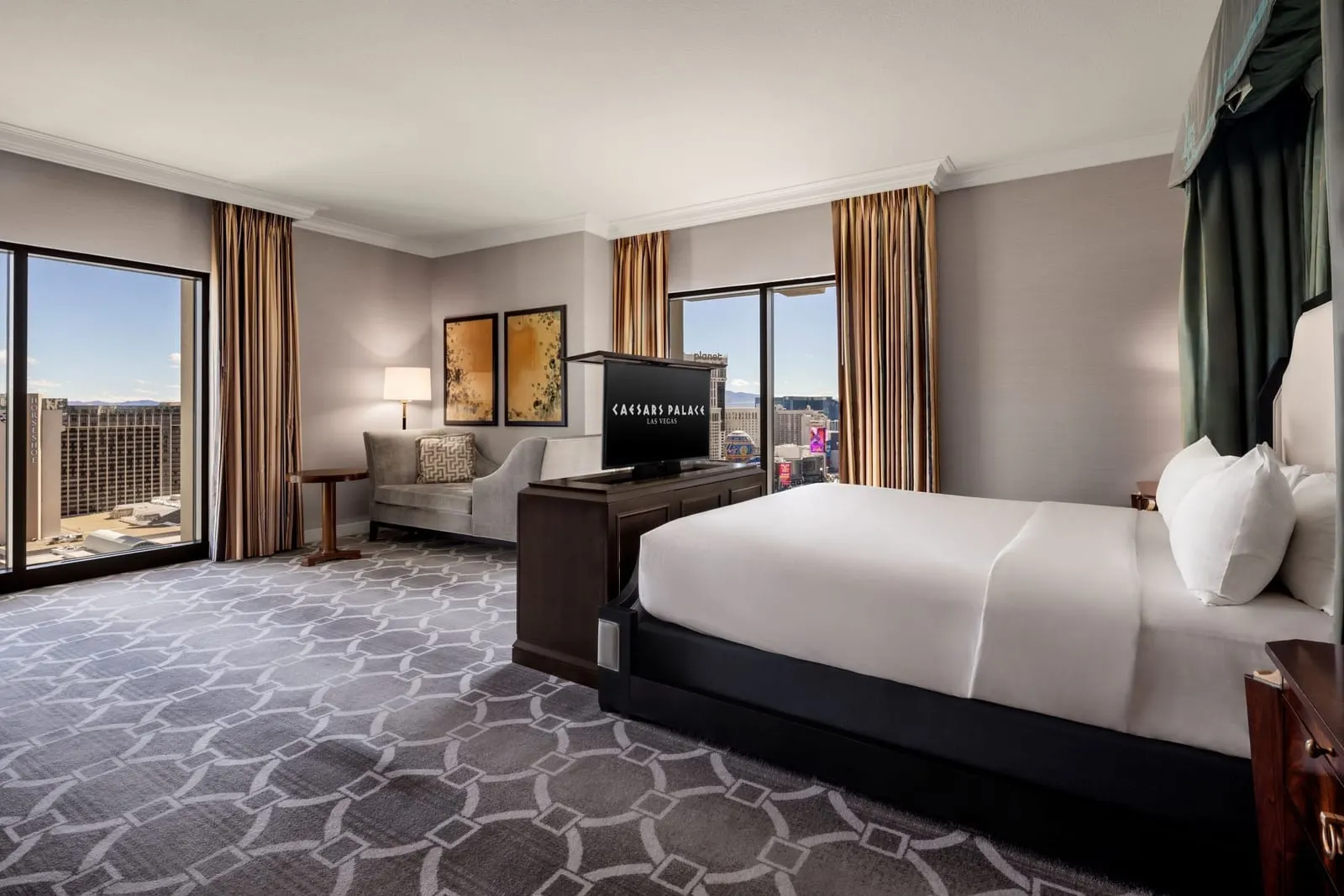 Augustus Premium Suite im Caesars Palace, wie die Suite vor dem Umbau 2026 aussah: ein Kingsize-Bett gegenüber einem Fernsehschrank, ein kleines Sofa und Fenster auf zwei Seiten