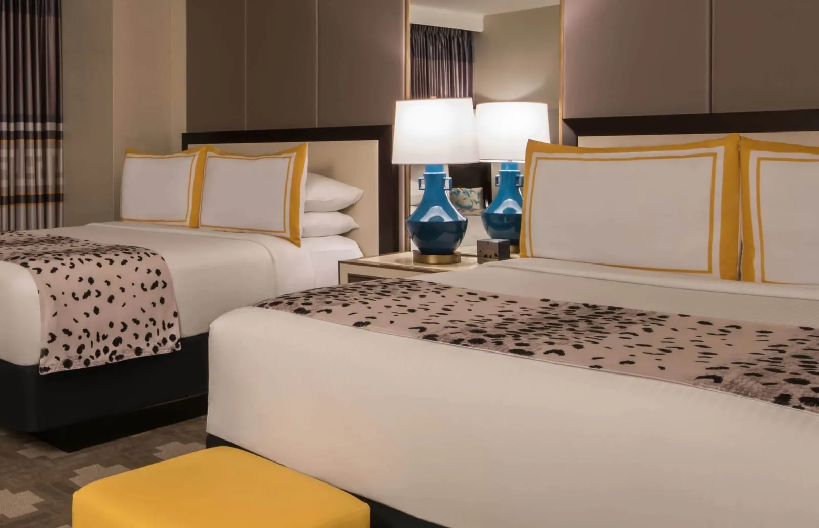 Julius Pool View Room im Caesars Palace: zwei Queensize-Betten mit Kissen mit Goldbesatz, blauen Lampen und einem gelben Polsterhocker