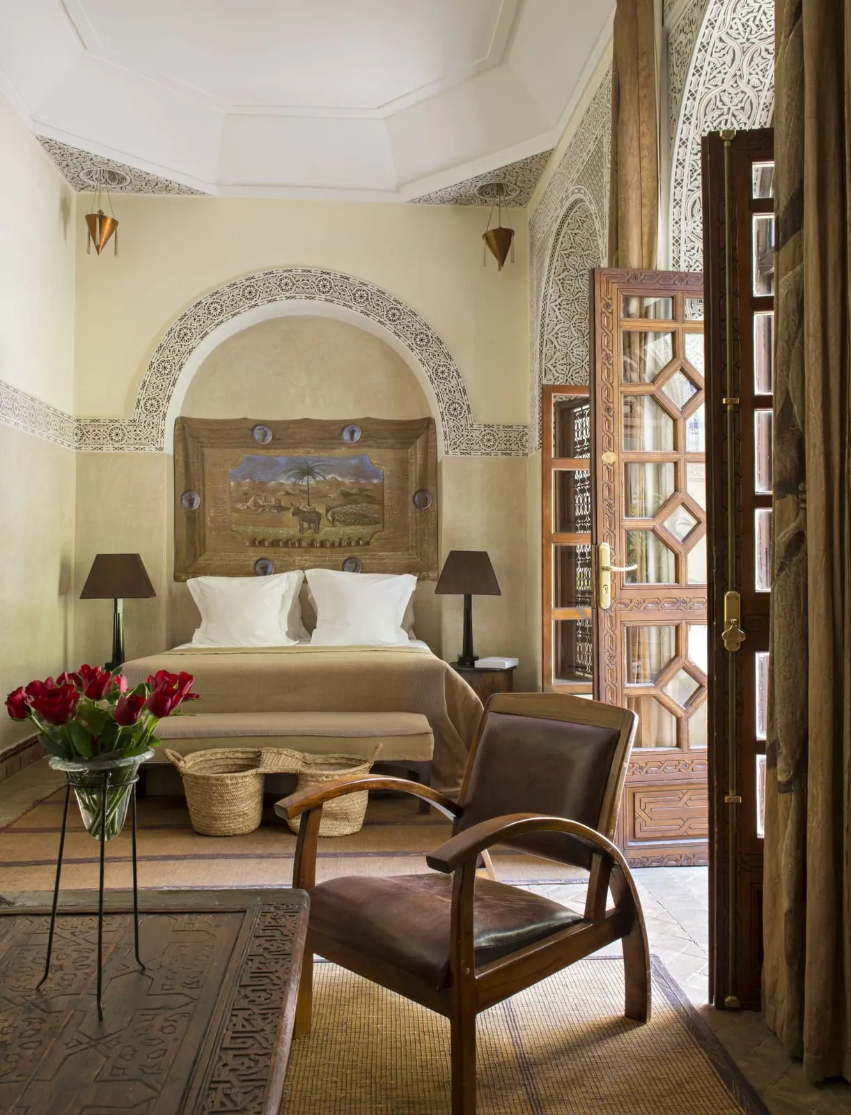 Deluxe Room at La Villa des Orangers: a double bed set in a carved plaster arch, with a leather armchair and carved wooden doors standing open.