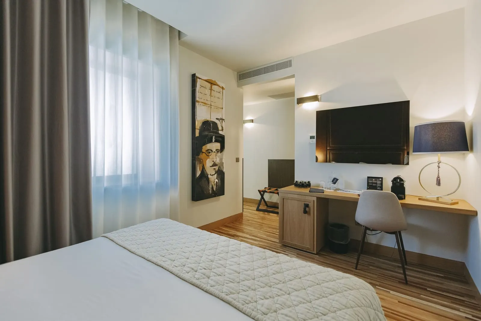 Classic Room at Torel Avantgarde: the bed, a desk with a chair, a wall television and a painted portrait by the window