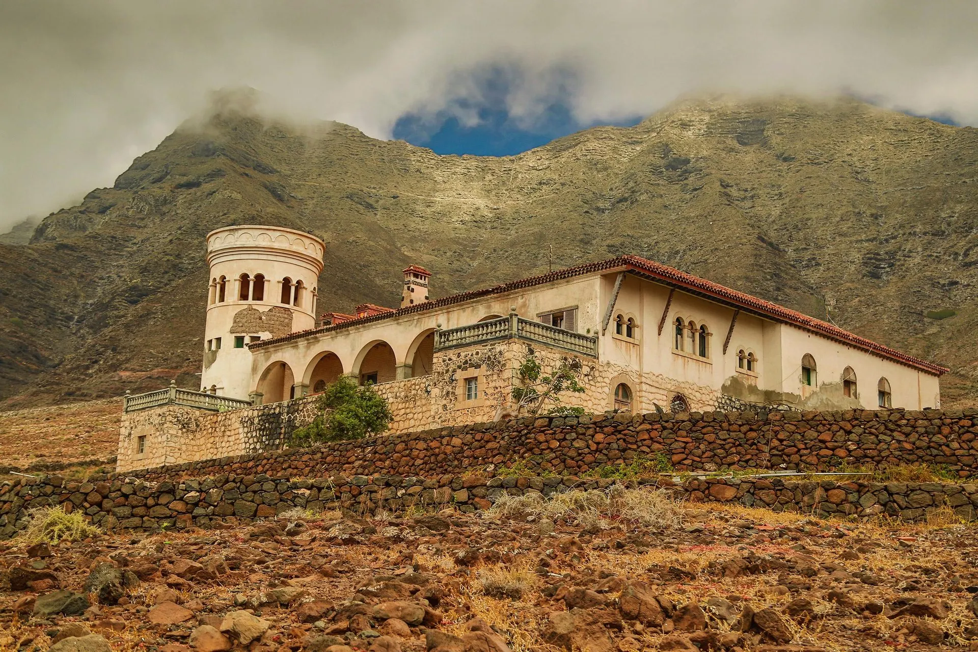 Villa Winter, a house with a round tower and arched terrace, below the cloud-capped Jandía mountains