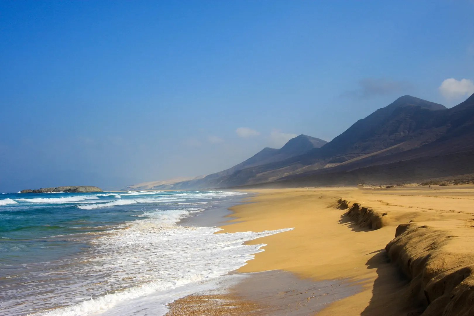 Waves breaking on Cofete beach, with a small islet offshore and the mountains behind