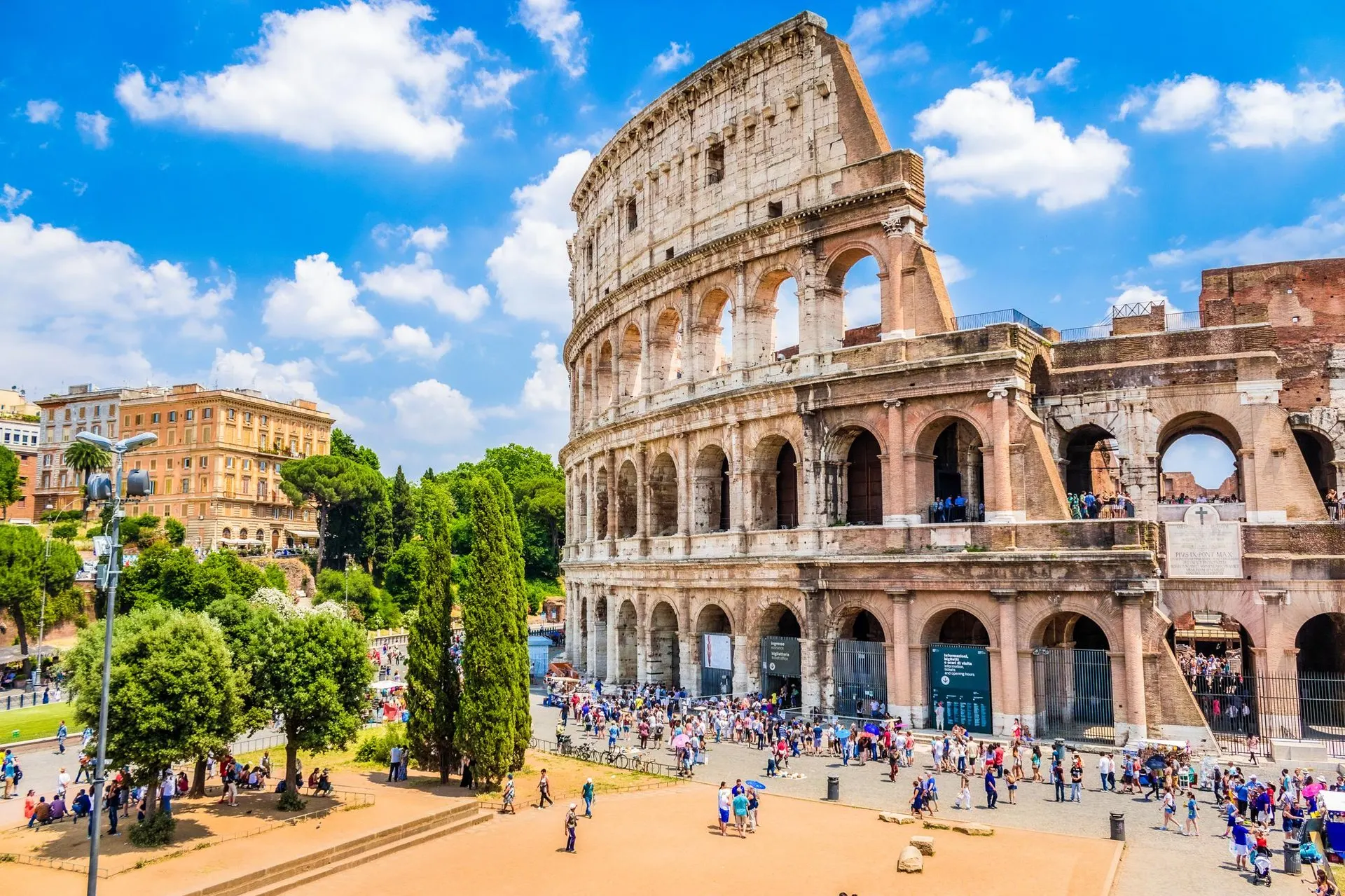 The Colosseum under a summer sky, with visitors on the square below