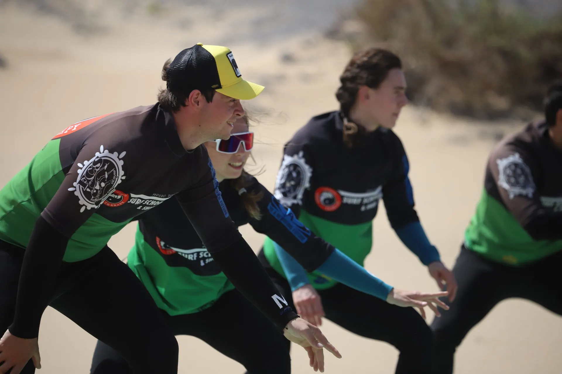 Learners in rash vests practise the surfing stance on the sand before going in the water