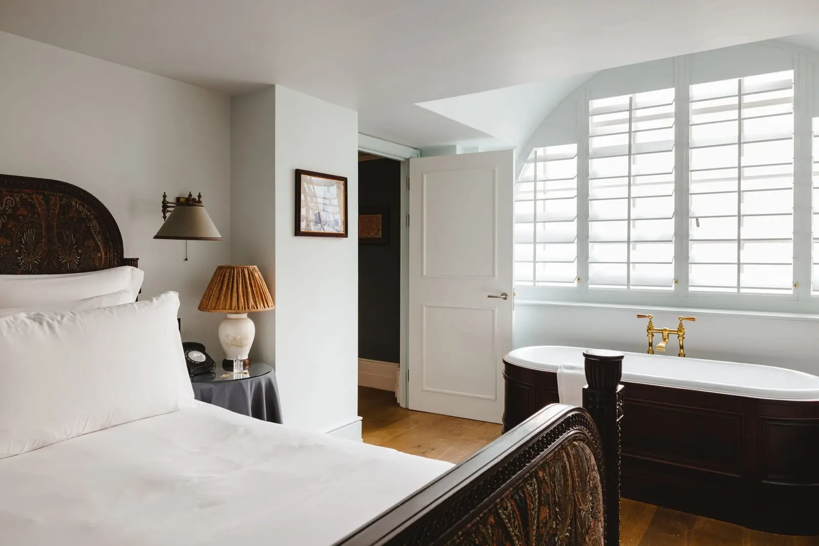 Two Bed Family Suite at The Ned: a bed and a roll-top bath below a shuttered window