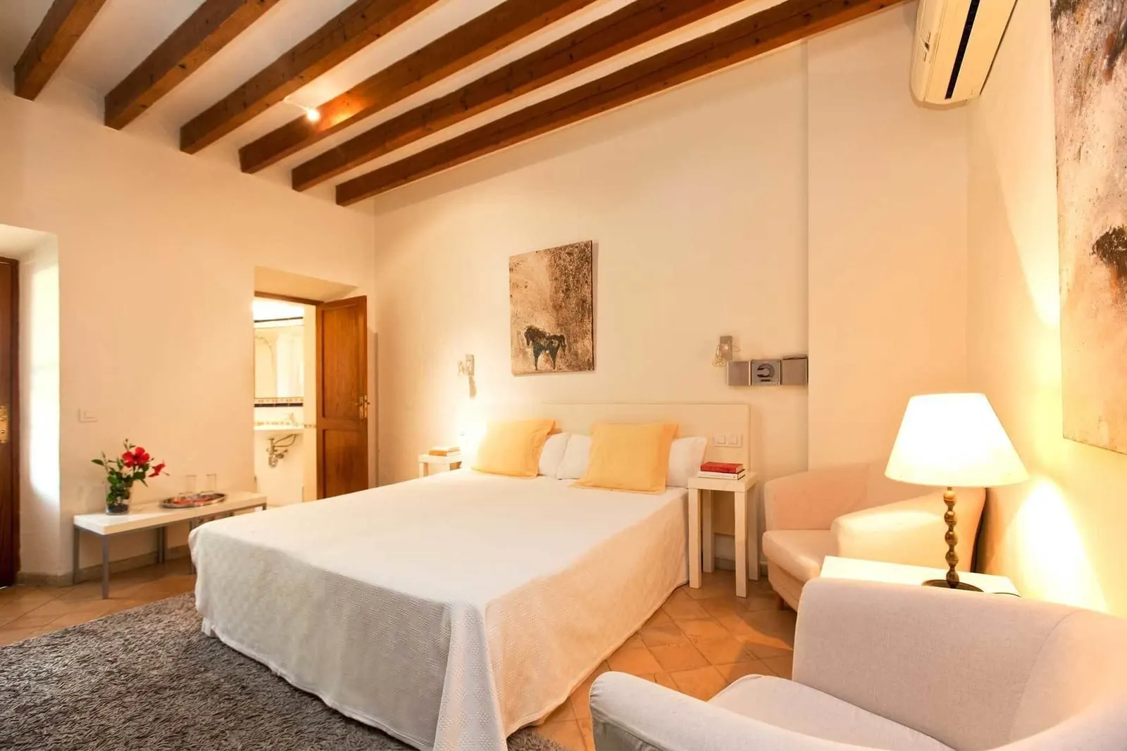 Habitación vista montaña y terraza privada at Fornalutx Petit Hotel: a double bed under dark wooden beams, two armchairs, a wall-mounted air conditioner and a doorway to the bathroom