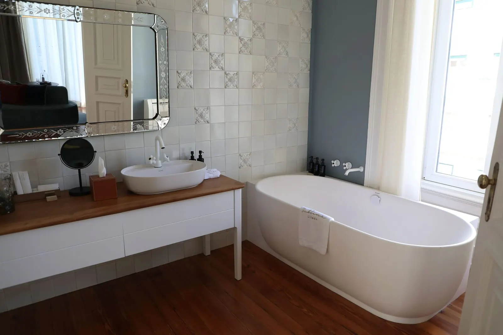 Sublime Suite bathroom at Sublime Lisboa: a freestanding bath by a tall window and a basin under a Venetian mirror