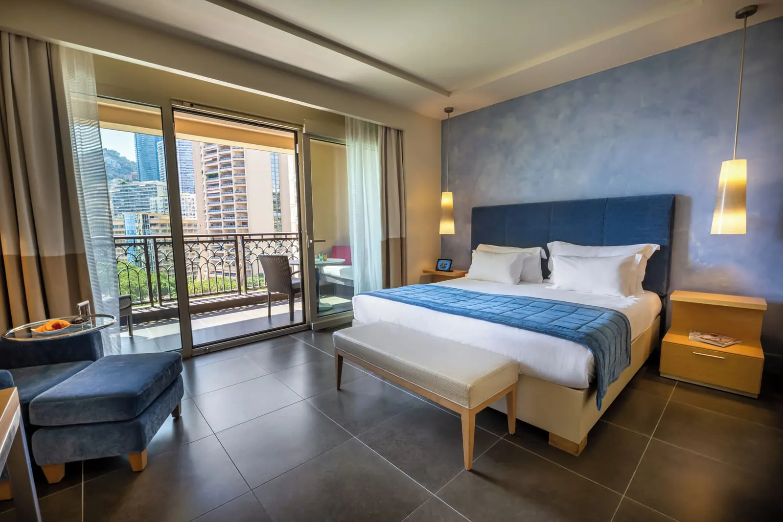 Deluxe Room seaside at Monte-Carlo Bay Hotel & Resort: the bed with a blue headboard and glass doors to the terrace