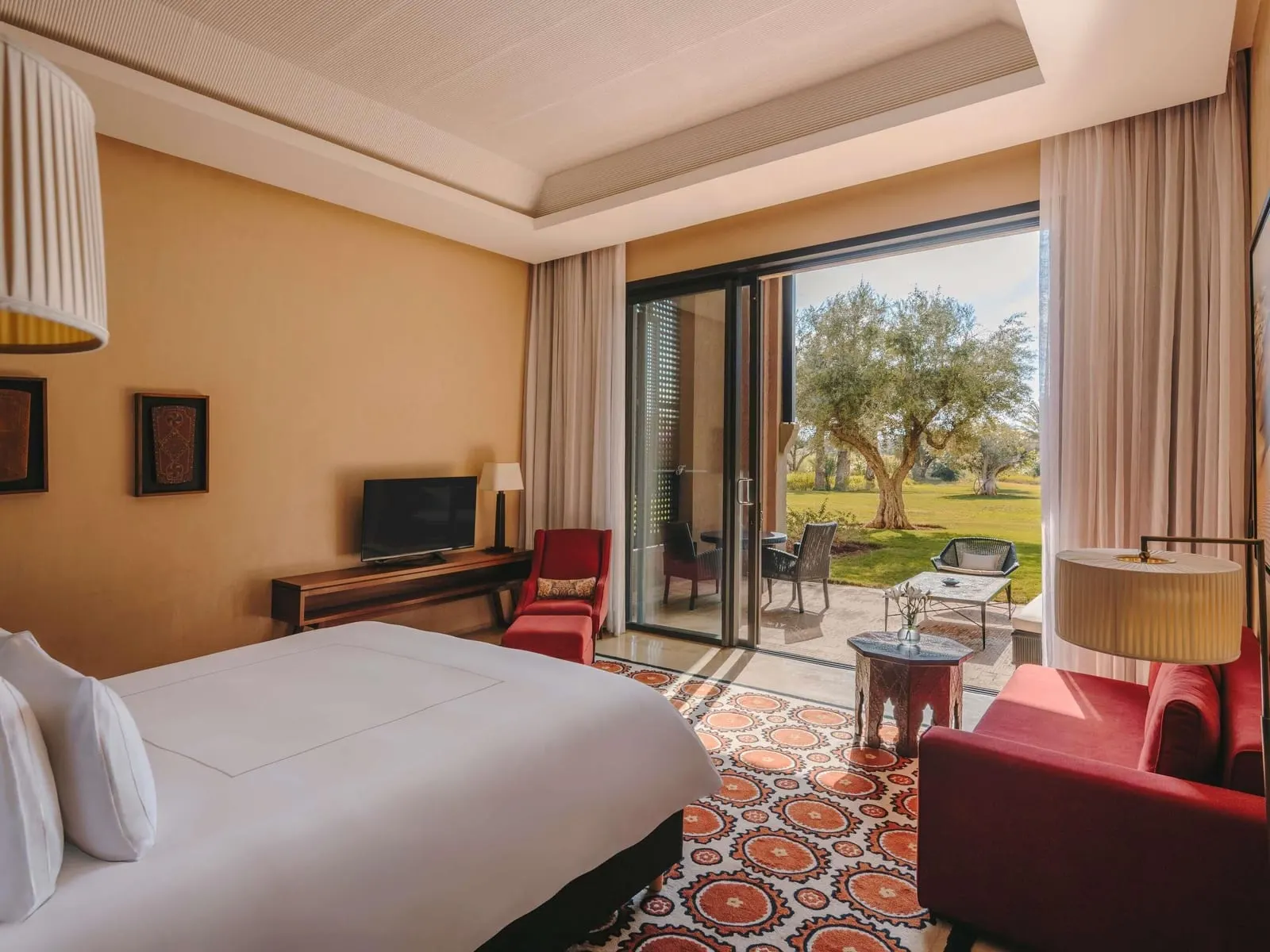 Junior Suite Garden View at Fairmont Royal Palm Marrakech: the bedroom with red armchairs and sliding doors onto a terrace and lawn with olive trees