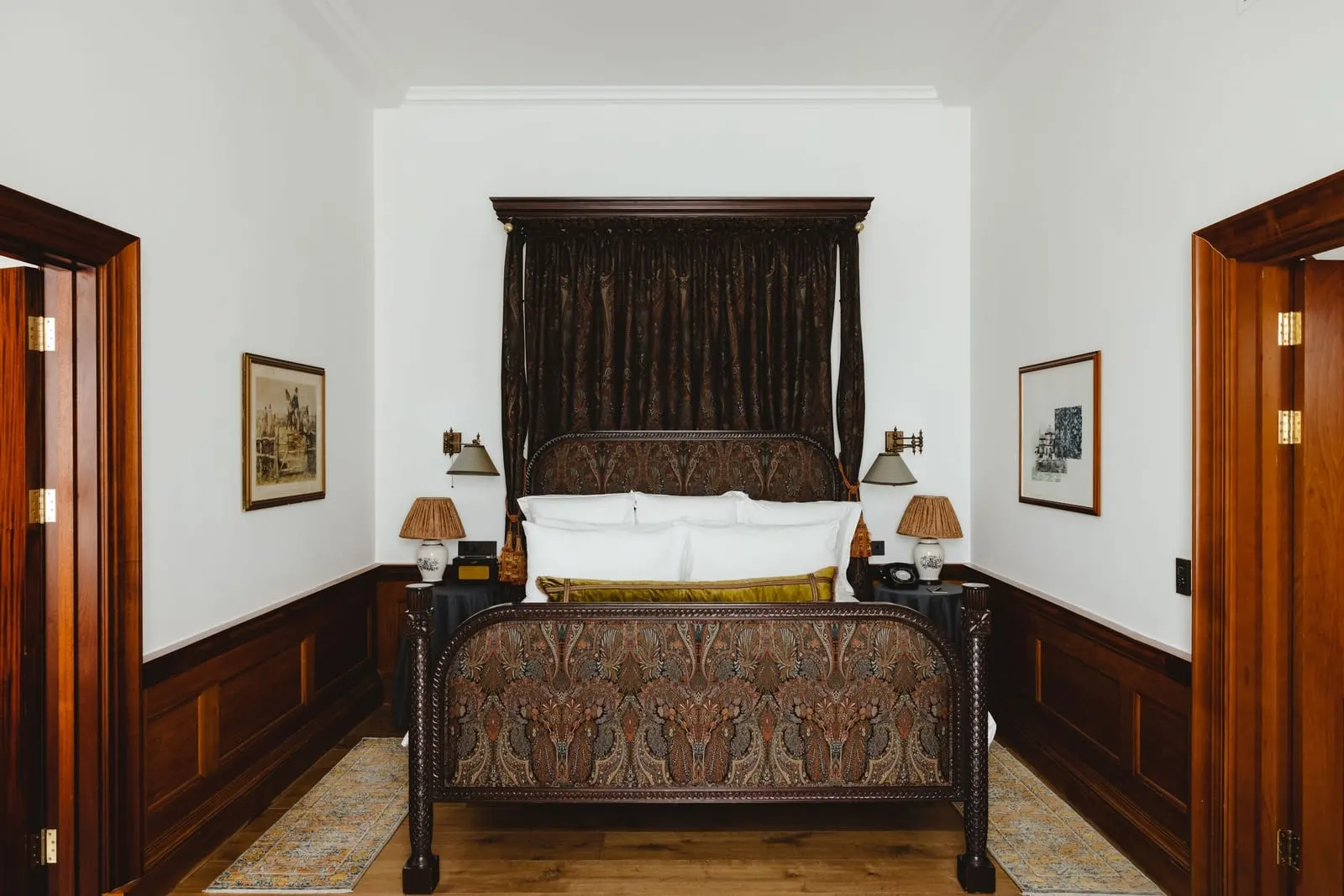 Heritage Suite at The Ned: a canopy bed with dark drapes between wooden doors, with panelling below white walls