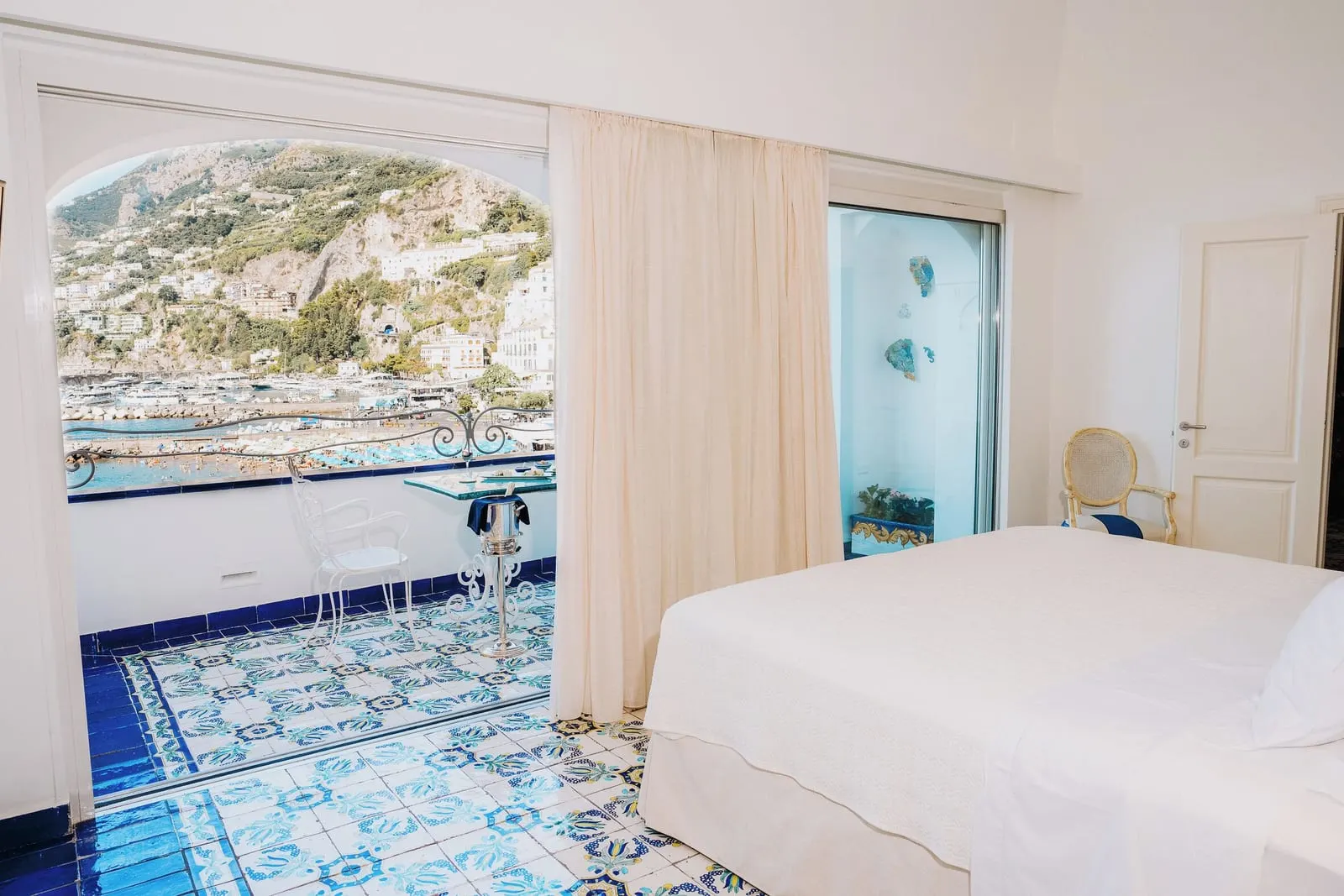 Suite Eolo（Hotel Marina Riviera）：青と白のマヨルカ焼きの床のダブルベッドと、タイル張りのパティオテラスへのアーチ形の開口部、テーブルと椅子