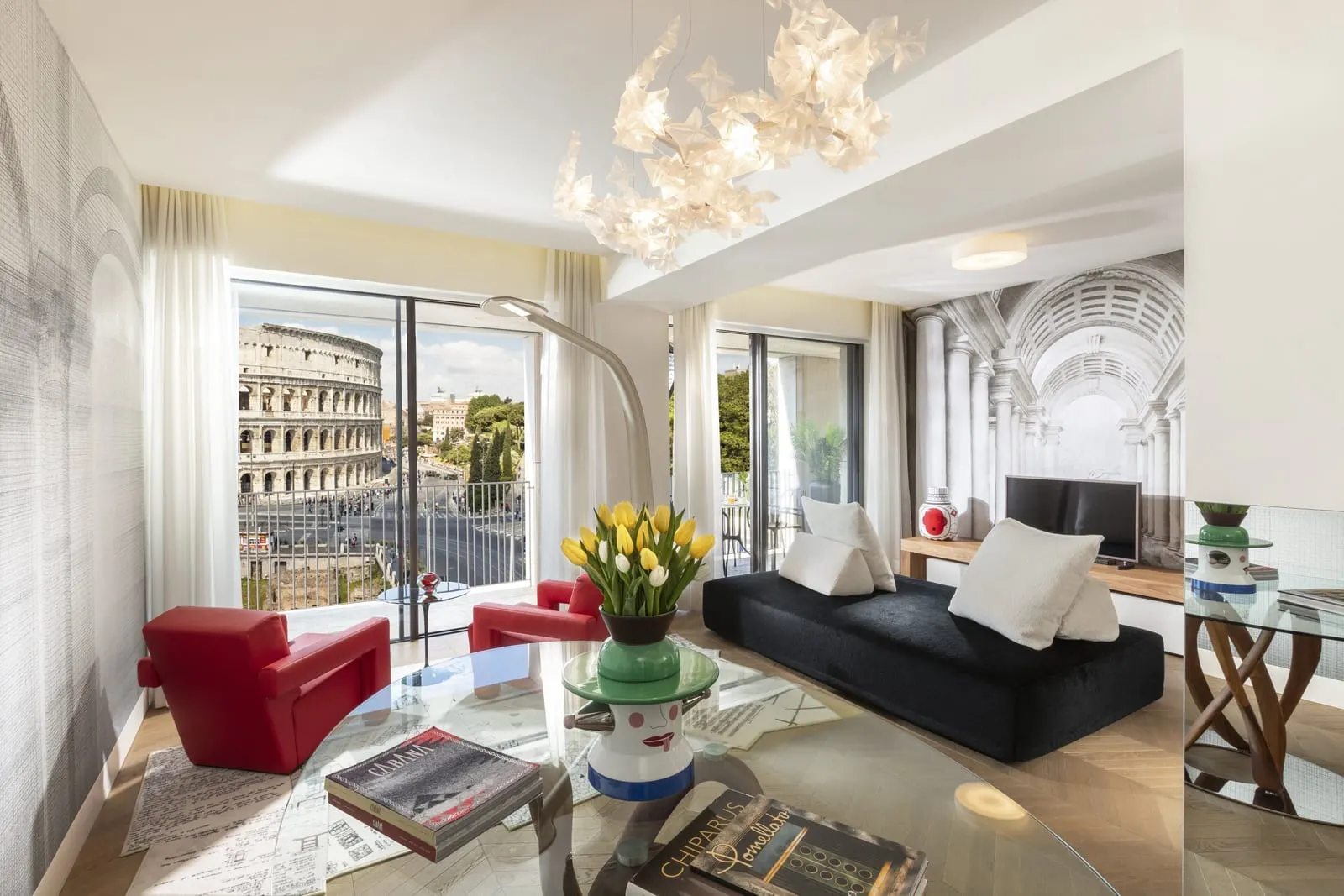 Grand View Gallery Suite at Palazzo Manfredi: the living room, red armchairs and a black sofa, the Colosseum outside