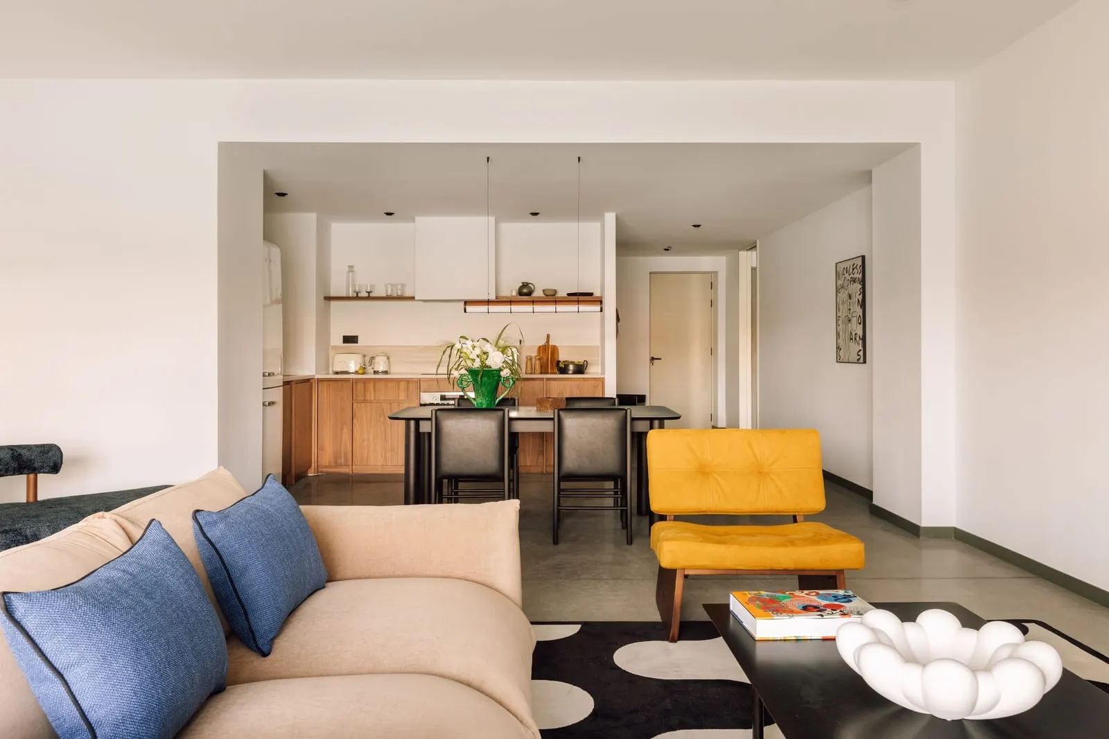 One Bedroom Suite at The Rebello: a sofa and a yellow armchair, with the dining table and kitchen beyond