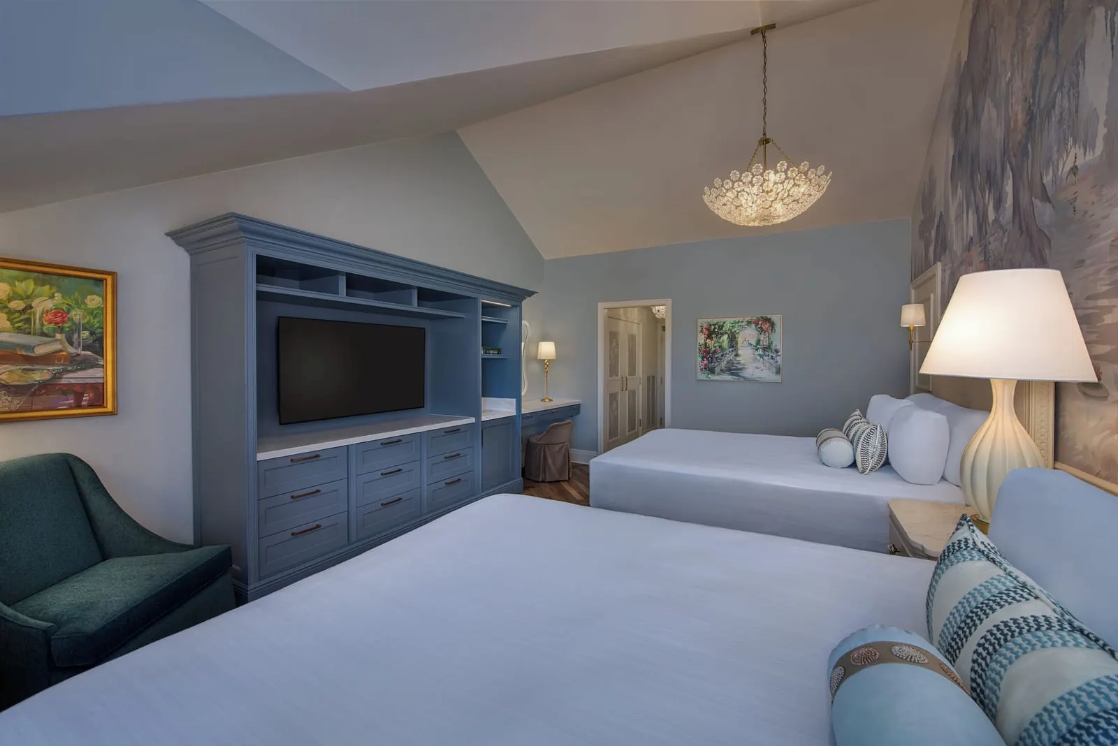 2 Bedroom Suite - Club Level Access at Disney's Grand Floridian Resort & Spa: a bedroom with two queen beds beside a painted landscape mural, a built-in blue television cabinet and a teal armchair under a sloped ceiling