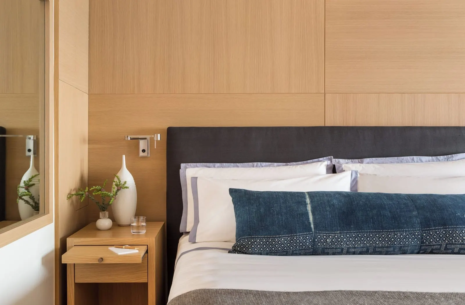 King Premier Ocean Front Room at Malibu Beach Inn: the head of a bed with a dark upholstered headboard, white and blue linen and a bedside table against oak panelling