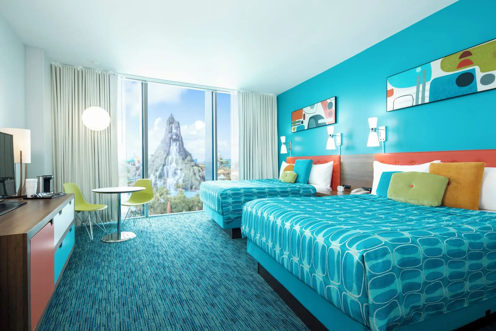 Volcano Bay View 2 Queen Beds at Universal Cabana Bay Beach Resort: two queen beds with orange headboards against a turquoise wall, a dresser with a television and a small round table with two green chairs by a floor-to-ceiling window