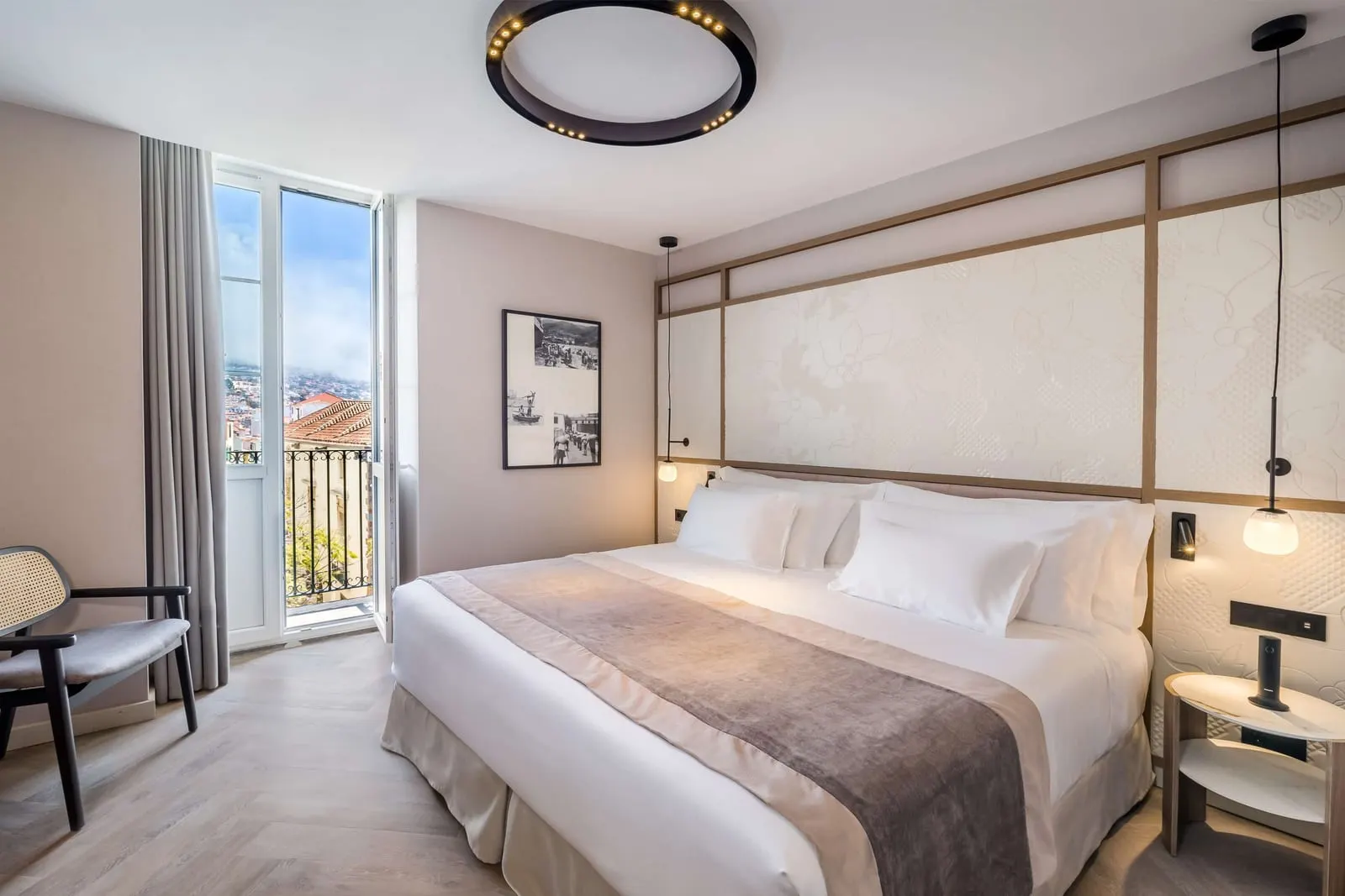 Deluxe City View at Barceló Funchal Oldtown: a double bed beside an open French window with an iron railing, looking over the rooftops of Funchal