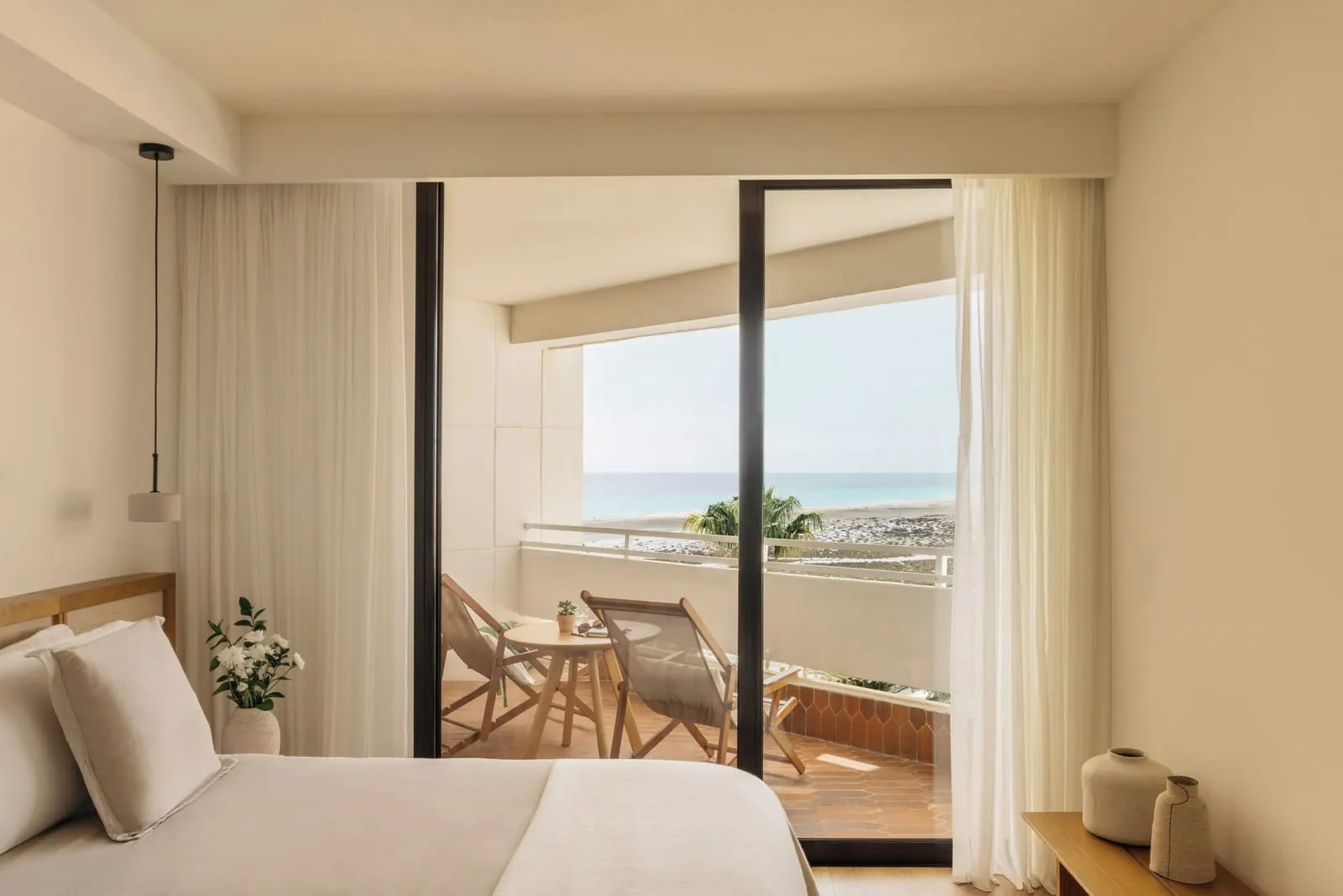 Premium Room Ocean View at Paradisus by Meliá Fuerteventura: a bed beside a glass door to a terrace with two folding chairs, with the sea beyond