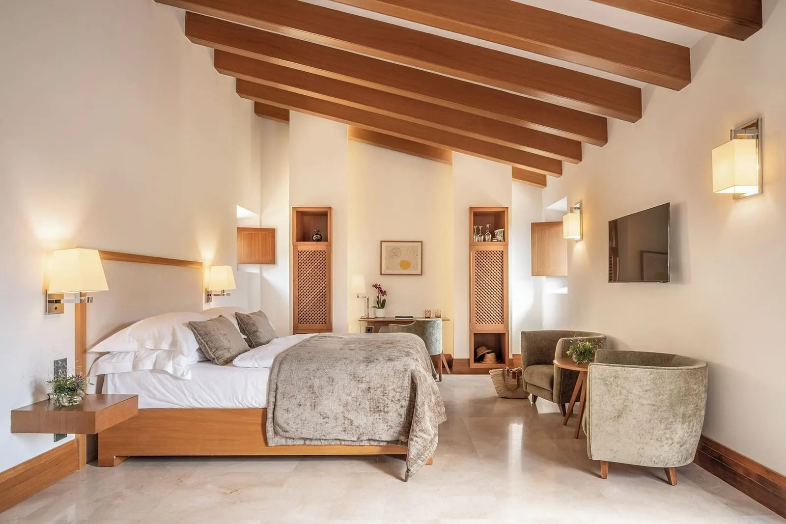 Terrace Deluxe im Castell Son Claret: ein Bett mit einem hellen Holzrahmen unter schrägen Holzbalken, zwei Samtsessel, ein Schreibtisch und ein Fernseher