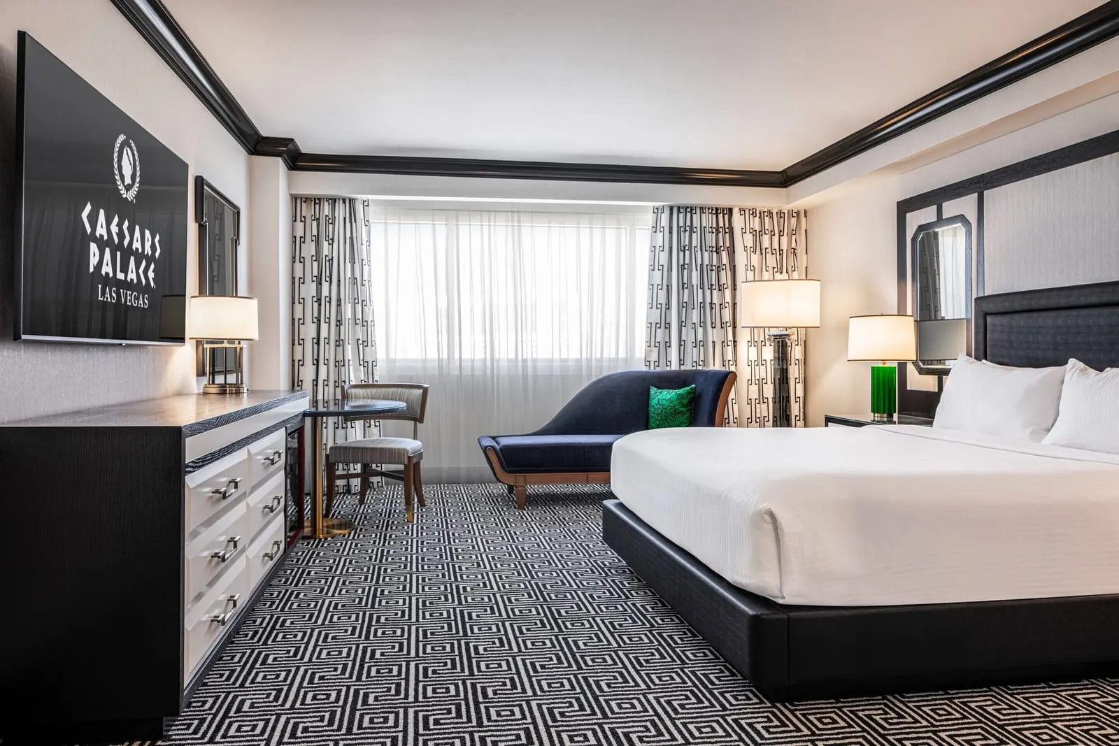 Colosseum Deluxe Room im Caesars Palace: ein Kingsize-Bett mit grünen Lampen, eine blaue Chaiselongue, ein kleiner runder Tisch und eine Kommode unter einem wandmontierten Fernseher