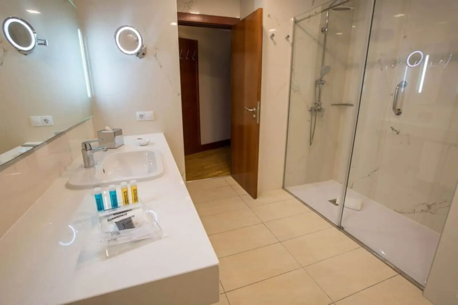 Double Sea View Room at Bull Reina Isabel & Spa: a bathroom with a walk-in shower behind a glass screen, a long white washbasin counter and two lit round mirrors
