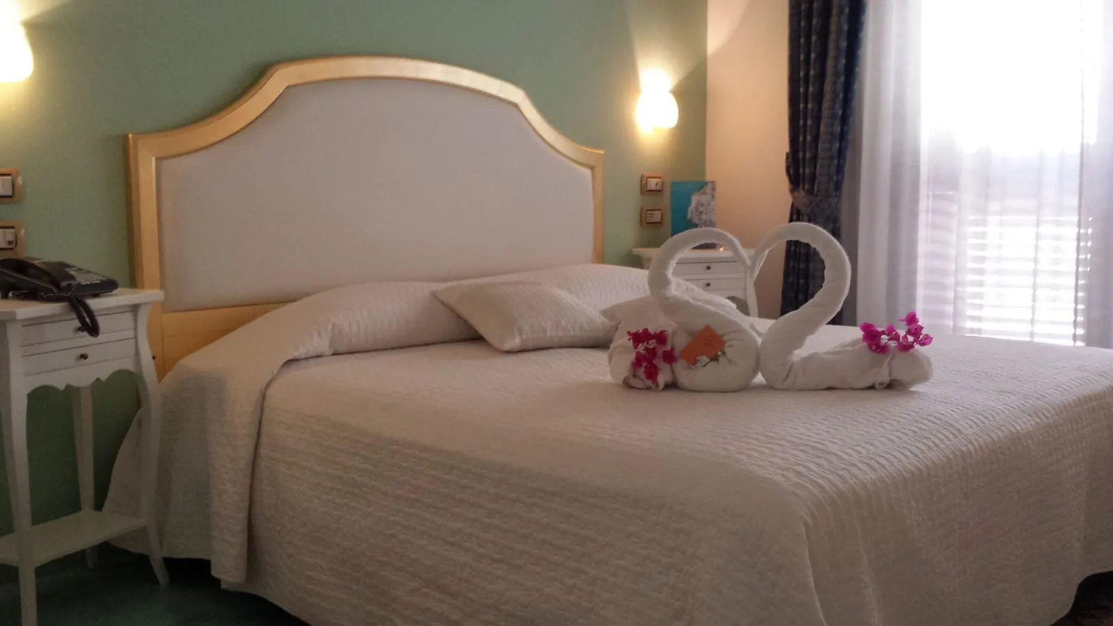 Superior Room at Hotel Santa Lucia: a double bed with a cream padded headboard against a pale green wall, with towels folded into swans