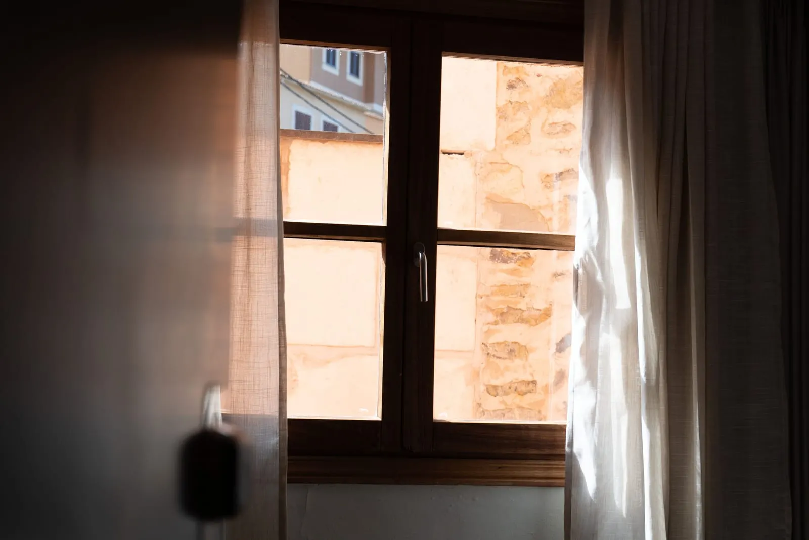 Cosy Room at Maristel Hotel & Spa: a wooden window with a sheer curtain, looking onto a sandstone wall and a neighbouring building