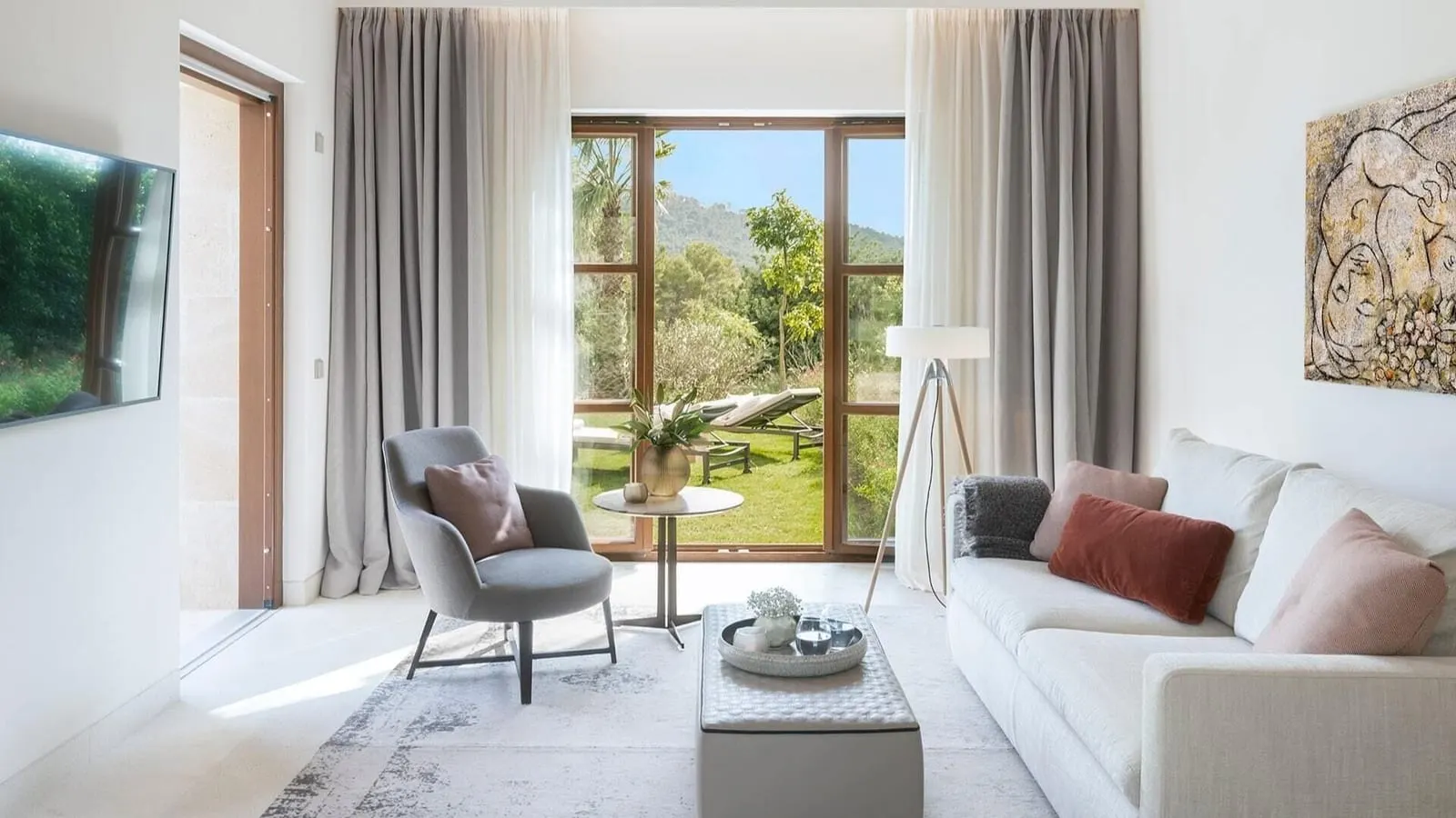 Pool Suite im Castell Son Claret: ein Wohnzimmer mit einem weißen Sofa, einem grauen Sessel und einem hohen Fenster zu einem Rasen mit Liegen