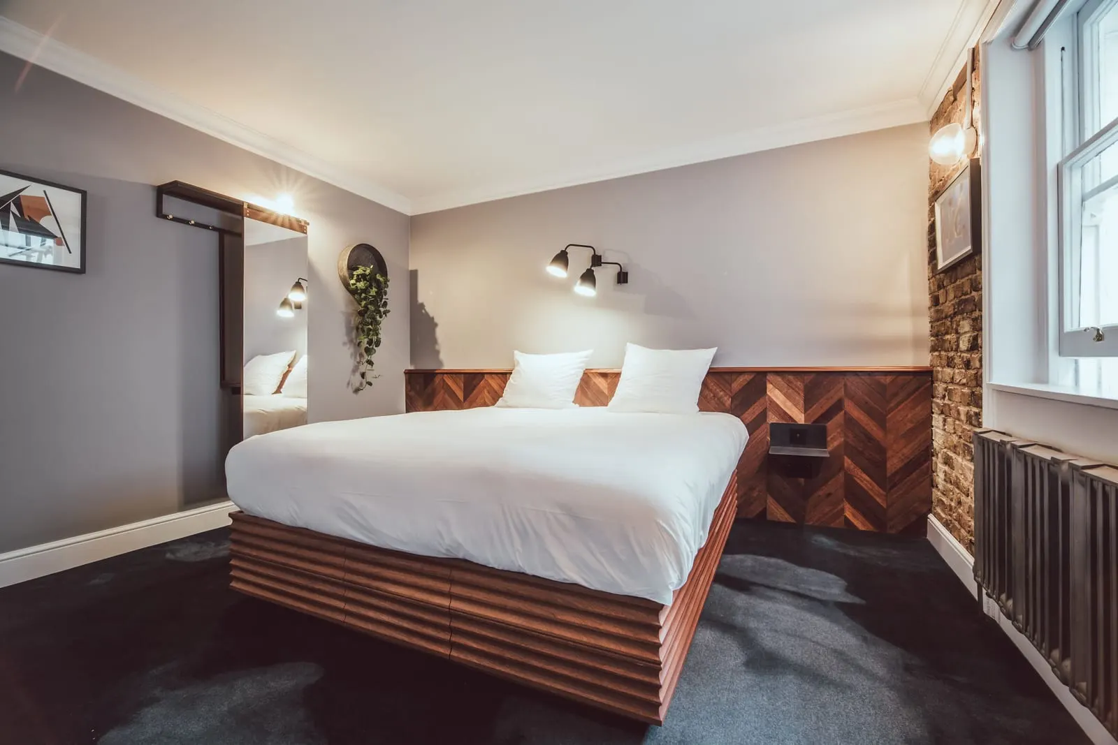 Comfy room at The Pilgrm: the bed on a wooden base, a herringbone wood wall, an exposed brick wall and a window