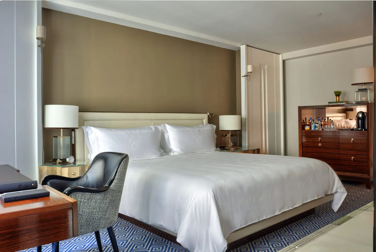 Superior Room at The Carlyle: a king bed with white linen, a black armchair and writing desk in the foreground, and a wooden drinks cabinet against the wall